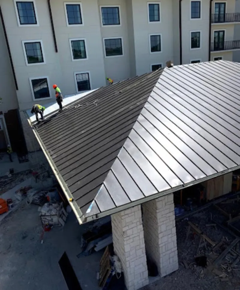 Crew installing standing seam metal roof panels on a commercial project in August